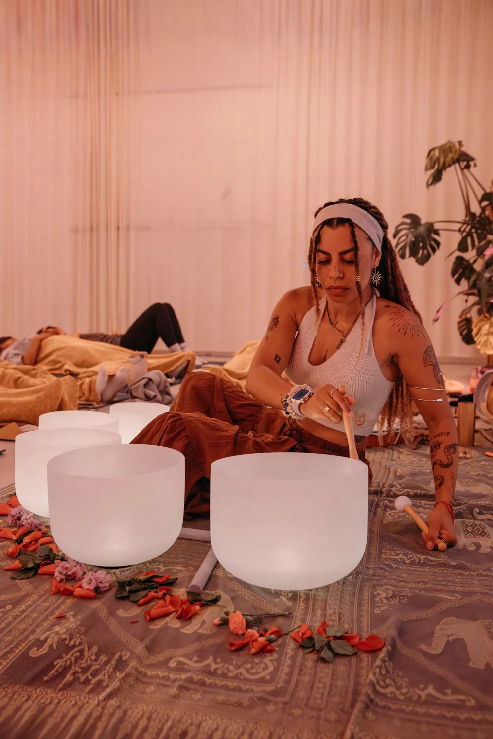 Maryrose playing crystal singing bowls at a sound bath, with guests resting under blankets